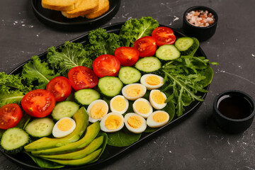 Plate of fresh salad with boiled quail eggs, soy sauce and sea salt on dark background, closeup