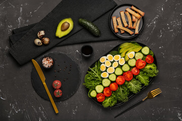 Composition with fresh salad, ingredients and cutlery on dark background