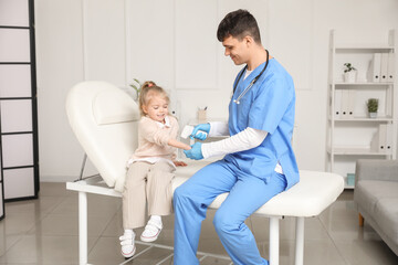 Fototapeta premium Male pediatrician measuring temperature of little girl with infrared thermometer in clinic