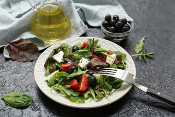 Plate of fresh vegetable salad with napkin, olives and fork on black background