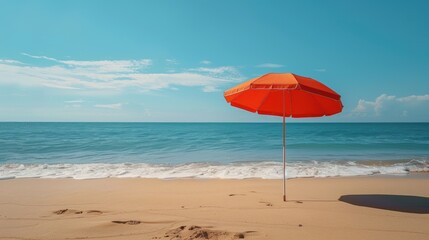 A bright orange beach umbrella providing shade on a sandy shore with gentle waves in the background, perfect for a summer day.