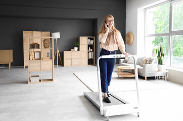 Young businesswoman talking by mobile phone on treadmill in office