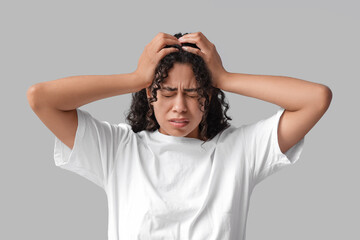 Young African-American woman having panic attack on grey background