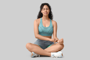 Sporty African-American woman checking pulse on grey background