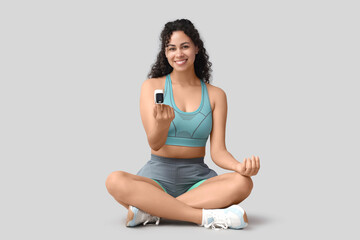 Sporty African-American woman checking pulse on grey background