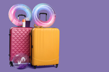 Inflatable rings, suitcases, sunscreen cream and passport with ticket on lilac background. Travel concept