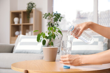 Woman pouring water from bottle into glass on table at home, closeup