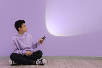 Teenage boy shining flashlight on lilac wall