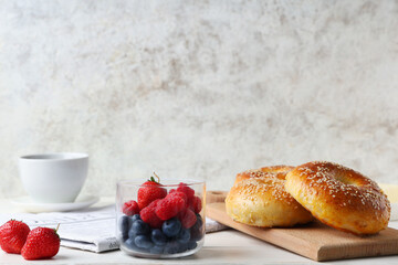 Board with tasty bagels and berries on white wooden table