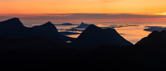 Panorama of sunset view over norwegian mountain islands. Luröyfjellet in the distance. Midnight sunset, dawn and sunrise in the arctic summer night. Norway coastline. Colours of Nordland, Helgeland