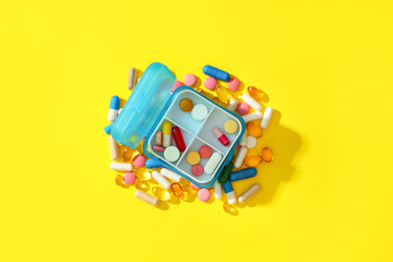 Obraz premium Blue plastic container with pills on yellow background. Top view