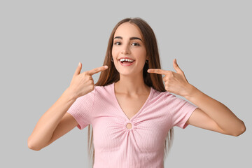 Young woman with diastema pointing at her teeth on light background