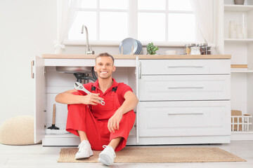 Male plumber with wrench fixing sink in kitchen