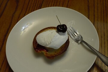 mini cherry pie on plate with whip cream and a cherry on top.