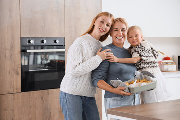 Young woman with her little daughter and mother holding baked potato near oven in kitchen