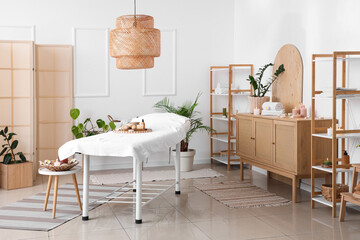 Interior of light spa salon with massage couch, burning candles and shelf units