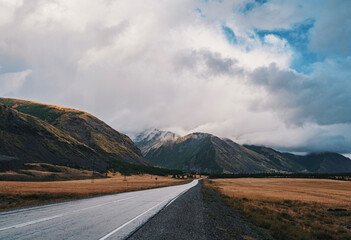 Majestic mountains under cloudy skies along a serene country road in autumn