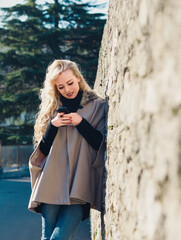 Young woman using smartphone app leaning on stone wall in europe