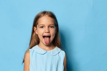 Playful little girl sticking out tongue against blue background with ample copy space © SHOTPRIME STUDIO