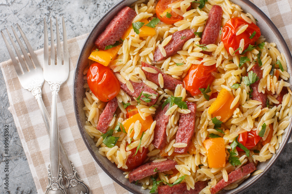 Wall mural one pot orzo pasta with fried salami sausage, bell pepper, garlic and tomatoes close-up in bowl on t