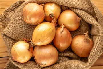 Fresh aromatic onion with jute bag on wooden table, macro, top view.