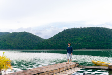 Fototapeta premium Young Asian man relax and enjoy outdoor lifestyle travel forest mountain on summer holiday vacation. Generation z guy relaxing on lake house balcony looking beautiful nature and breathing fresh air
