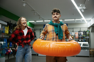 Happy joyful couple shopping at sportive store choosing inflatable ring