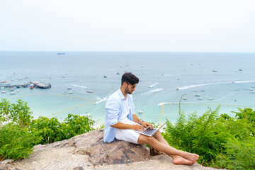 Caucasian man sitting on mountain peak remote working online corporate business financial on laptop computer. People enjoy outdoor lifestyle travel tropical island on summer beach holiday vacation.