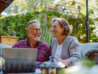Elderly couple laughing together while using a laptop outdoors