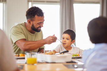 Lunch, family and father feeding son at dining room table in home for meal or social gathering. Eating, food and help with smile of happy people in apartment together for bonding, diet or nutrition