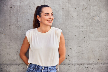 Portrait of happy mid adult woman looking away standing against concrete wall