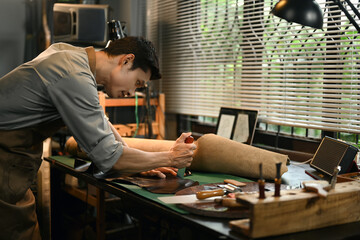 Focused male tailor working meticulously in a leather workshop. Small business and handmade concept