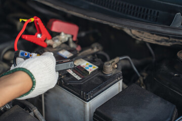 Close-up of mechanic holding voltmeter to check voltage car battery energy problem for service maintenance. Car mechanic noting repair parts during open car hood engine repair unrecognisable