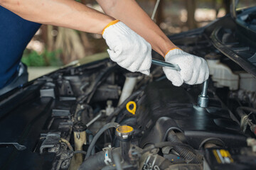 Close-up of Car mechanic noting repair parts during open car hood engine repair unrecognisable man wearing gray glove inspecting car engine and interior of hood of car. at garage. 