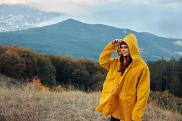 A woman in a yellow raincoat enjoying breathtaking mountain view on top of the hill during travel expedition