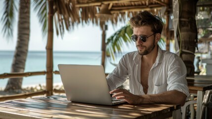 Young handsome professional man working on a laptop at a beachside cafe, digital nomad and remote work concept .