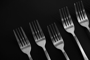 Stainless forks placed orderly and one stands out with a dark theme. Close-up stainless fork texture on black background. Stainless tableware, metal, table setting, and still-life on black concepts.