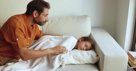 Loving caring dad tucking up cute child girl sleeping on home couch, stroking child under warm plaid, keeping silence. Calm adorable asleep preschool girl ling on sofa with head rested on pillow