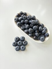 Delicious juicy blueberries isolated on white background. Black blueberries on white saucer. Tasty and healthy food