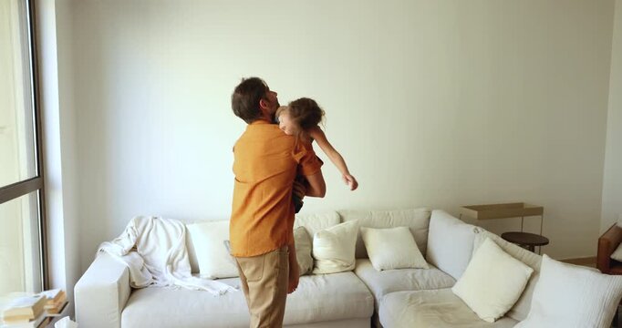 Cheerful strong Latin dad lifting little daughter kid up in air, rocking and holding child in arms. Happy girl and loving daddy playing active games in home living room, having fun together