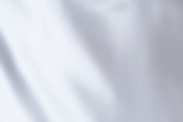 White satin fabric background with copy space. Abstract cloth background with simplicity, luxury, and smooth concepts. Rippled white-grey fabric texture for wallpaper, background, and silk backdrop.