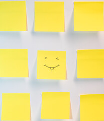 A yellow piece of paper with a smiley face drawn on it. The paper is placed next to other yellow pieces of paper