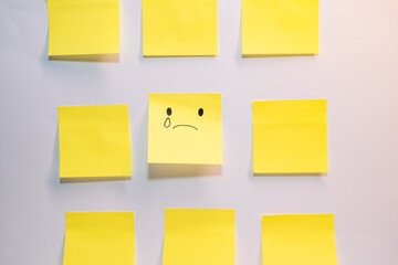 A yellow piece of paper with a sad face drawn on it is surrounded by other yellow pieces of paper