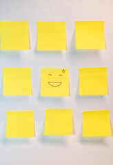 A yellow post it with a smiley face on it. There are nine other yellow post it's on a white background