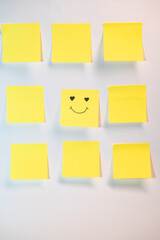 A yellow post it with a smiley face on it. There are nine other yellow post it's on a white background