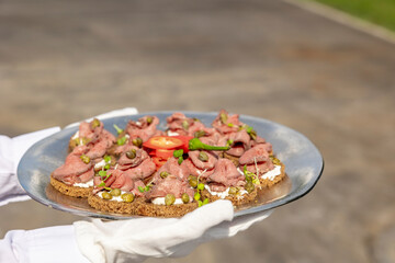 The waiter serves croutons with veal jerky with cream cheese and capers