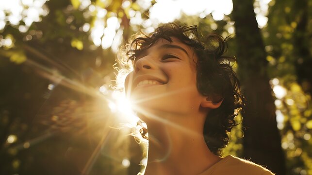 A close-up of a person's face with a genuine smile, sunlight streaming through the trees behind them.