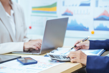 Two young Asian businesswomen sit at a table, engaged in a meeting.examine graphs and discuss capital investment strategies, showcasing their expertise and collaborative approach to business growth.