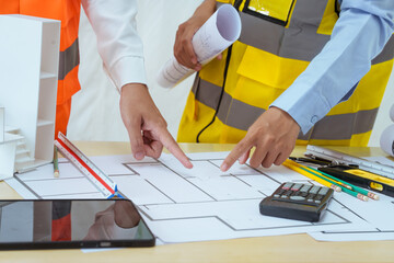 Two young women work at a desk, meticulously designing and drawing plans for building a house. As...