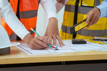 Two young women work at a desk, meticulously designing and drawing plans for building a house. As...